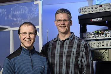 Two professors standing in front of a rack of equipment