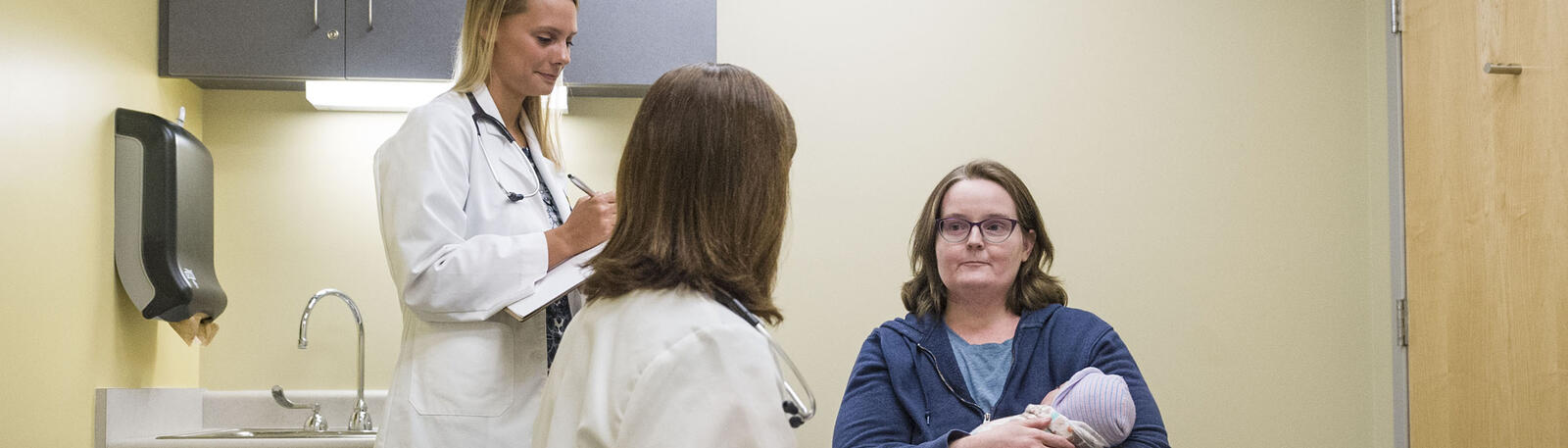 photo of a resident, physician, mother, and baby in an exam room