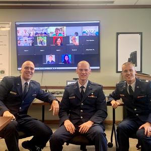 Three men in military uniform seated in front of a video conference call in a conference room