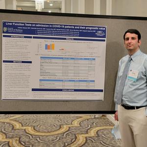 Ammar Ahmad stands beside his conference poster, Liver Function Tests on admission in COVID-19 patients and their prognostic value