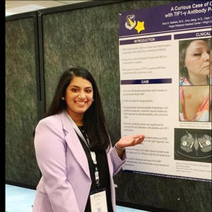 A student poses in front of their research poster at a conference.
